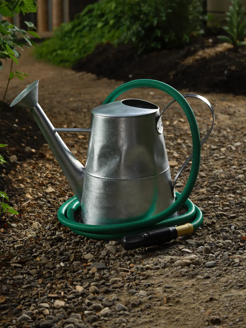 Verzinkte Giesskanne, Gartenschlauch und Tropfbewässerungs-Anschluss auf einem Kiesweg